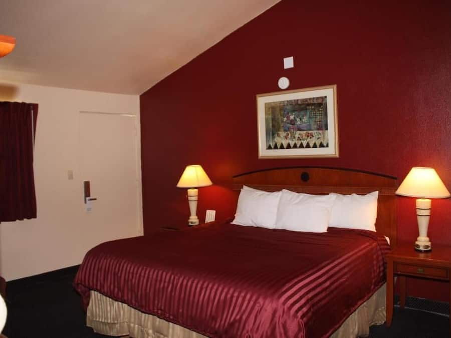 A hotel room with a large bed, two bedside lamps, a door, and a framed picture on the wall.