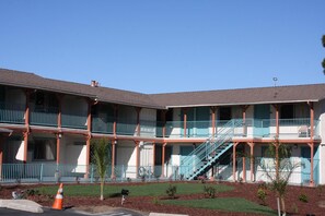A multi-story hotel with balconies, a central staircase, and a well-maintained lawn.