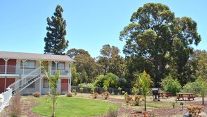 A two-story building with a balcony, surrounded by a landscaped garden with trees and shrubs. - Budget Inn (San Luis Obispo)