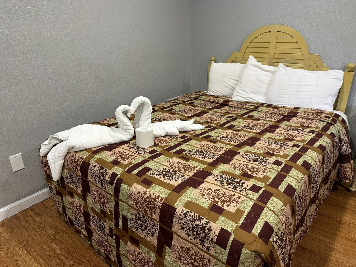 A bed with a patterned quilt, a wooden headboard, and a towel shaped like swans.