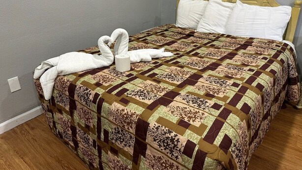 A bed with a patterned quilt, a wooden headboard, and a towel shaped like swans. - Budget Inn (San Luis Obispo)