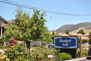 A sign for Budget Inn with a clear view of the surrounding area including a tree, flowers, and a hilly landscape in the background. - Budget Inn (San Luis Obispo)