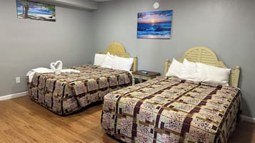 Habitación de hotel con dos camas, cada una con cubrecama estampado con motivos florales, una mesita de noche y un cuadro colgado en la pared que representa un atardecer sobre el océano.