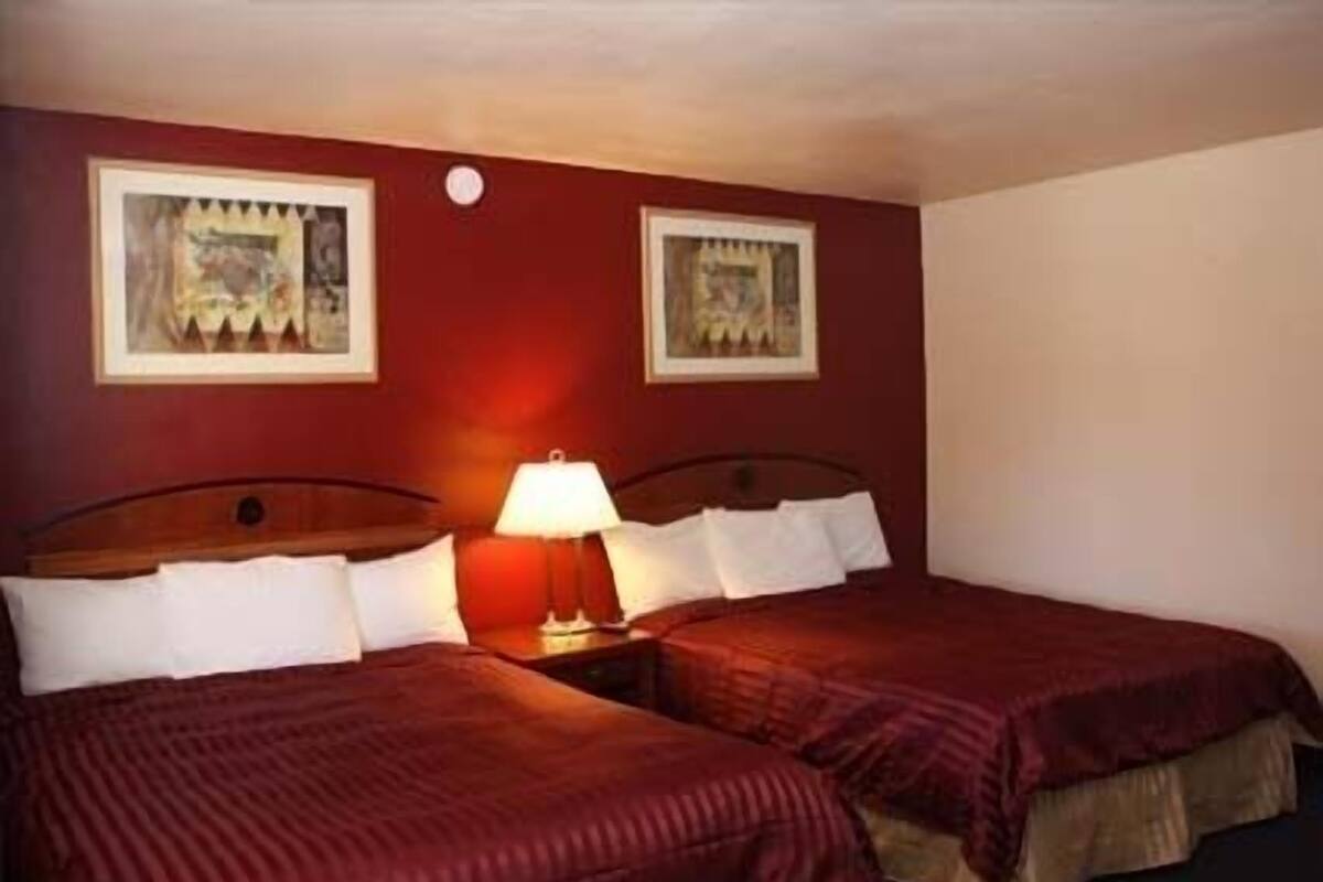 A hotel room with two beds, each with red bedding, a nightstand with a lamp, and two framed pictures on the wall.