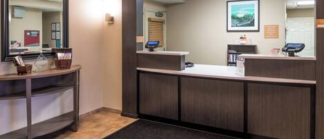 A reception area with a reception desk, a large mirror, a digital kiosk, and a small waiting area with a bench and magazines.