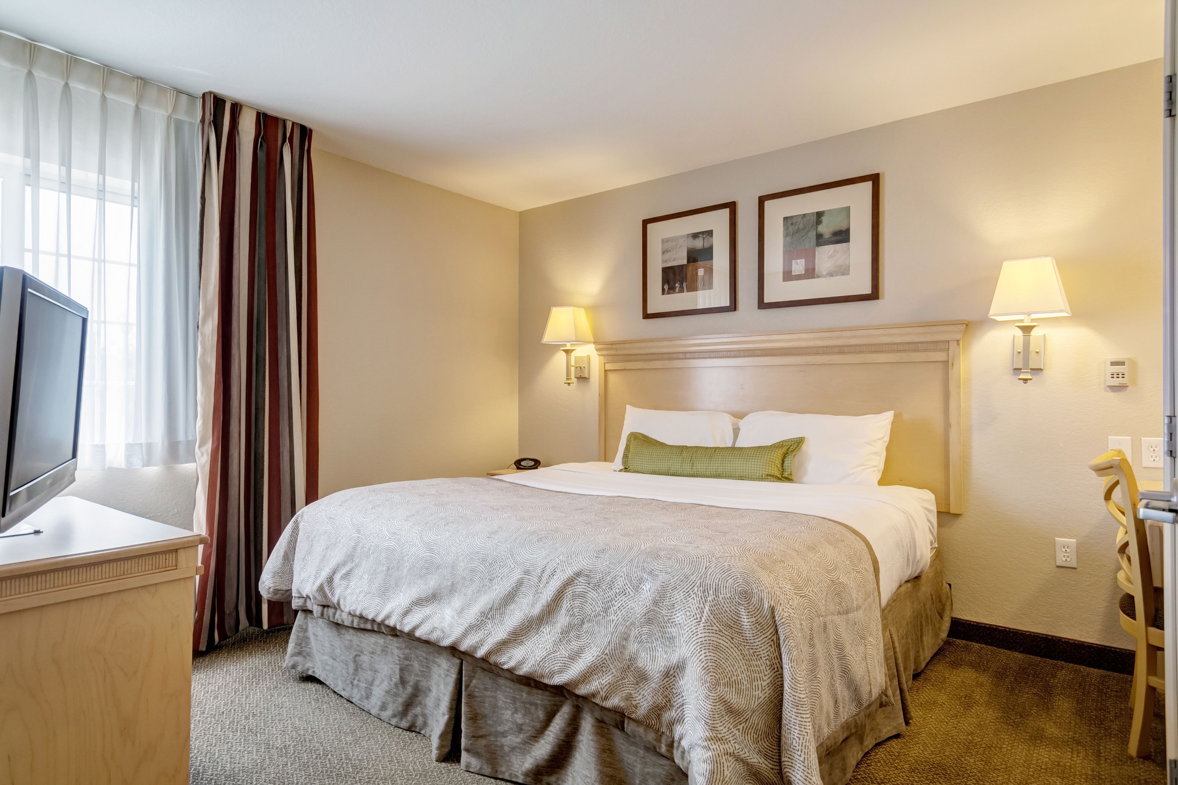 A hotel room with a bed, bedside lamps, a TV, and a desk.
