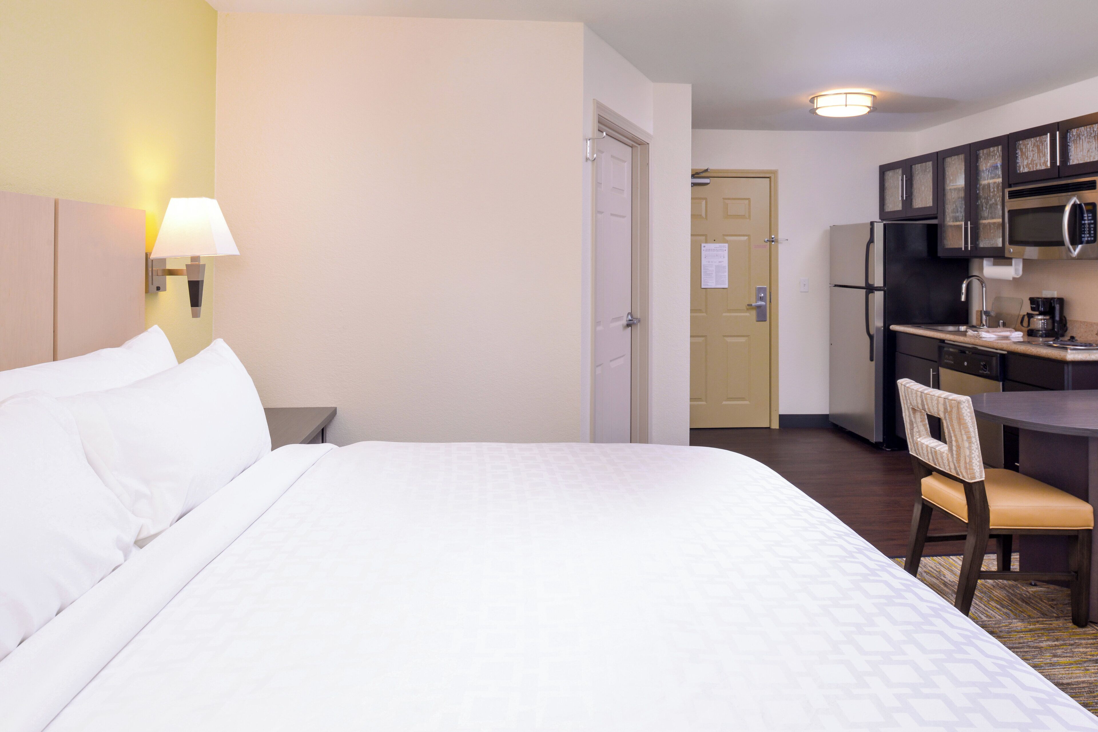 A hotel room with a bed, a desk, a chair, a microwave, and a refrigerator.