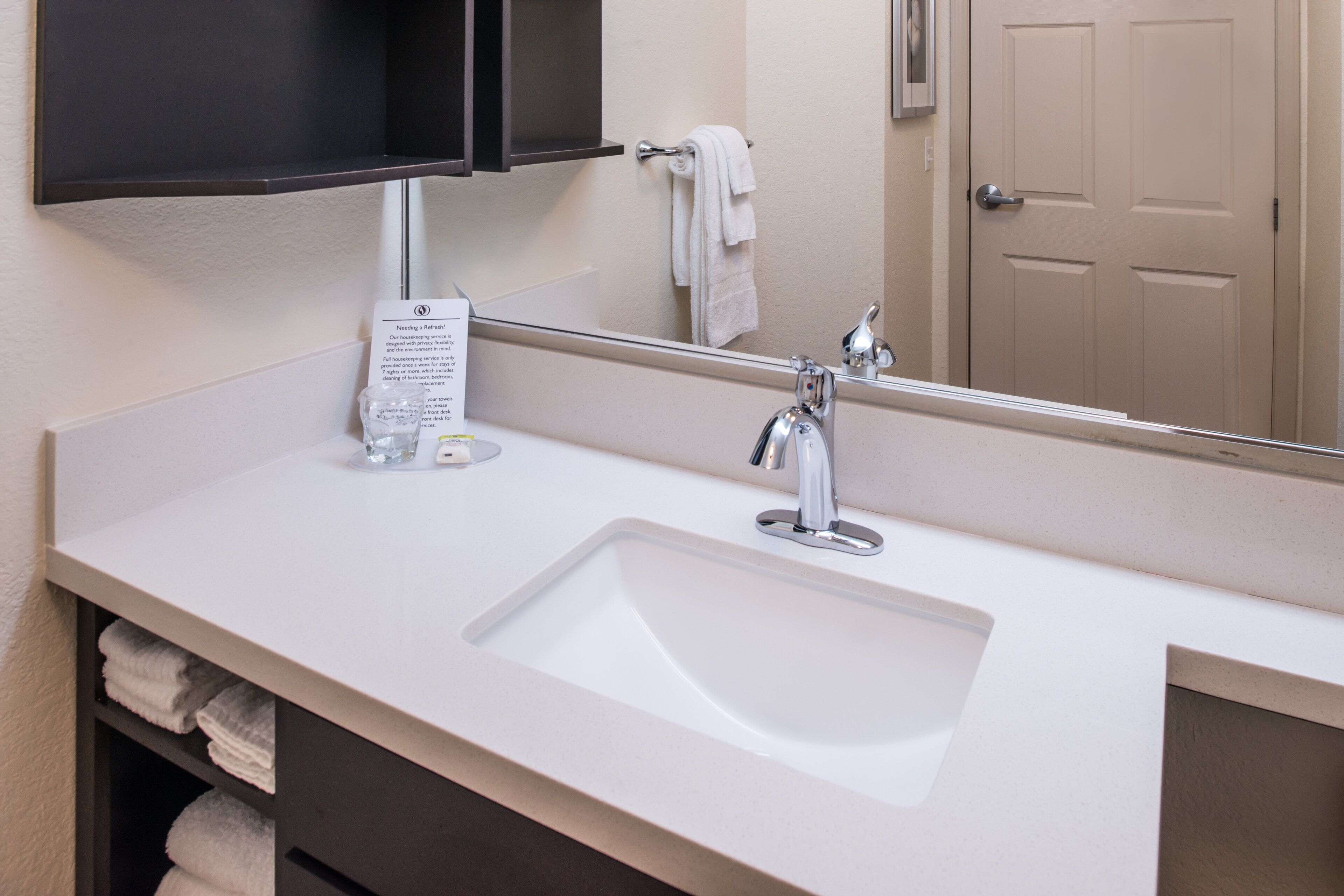 A hotel bathroom with a white sink, a mirror, a towel rack, and a door.