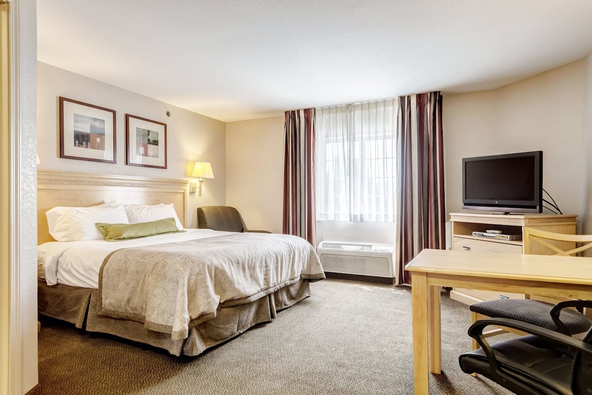 Ett hotellrum med en säng, ett skrivbord, en stol, en tv och ett fönster med gardiner.
