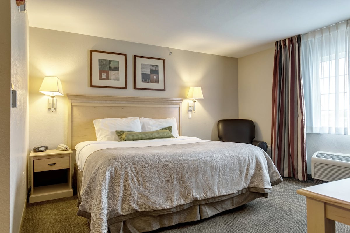 Ett hotellrum med en säng, två sänglampor, en stol, ett skrivbord och ett fönster med gardiner.