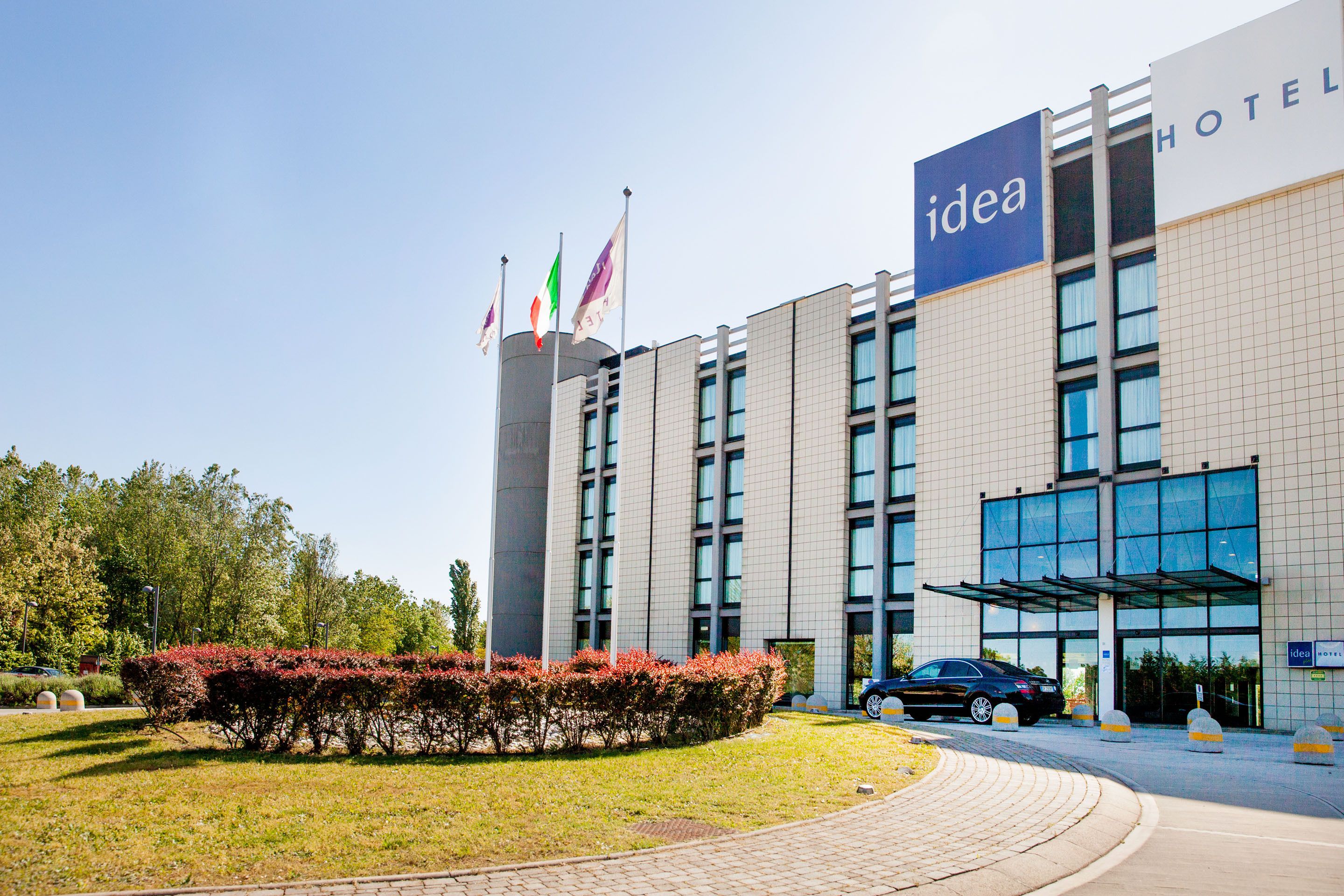 A modern hotel with a prominent 'idea' sign, a parking area, and a well-maintained garden.