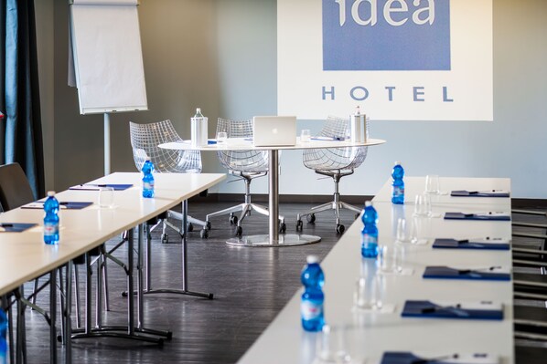 A conference room with a long table, chairs, a laptop, and water bottles. A projector screen displays "idea HOTEL". - Idea Hotel Milano San Siro (Milan)