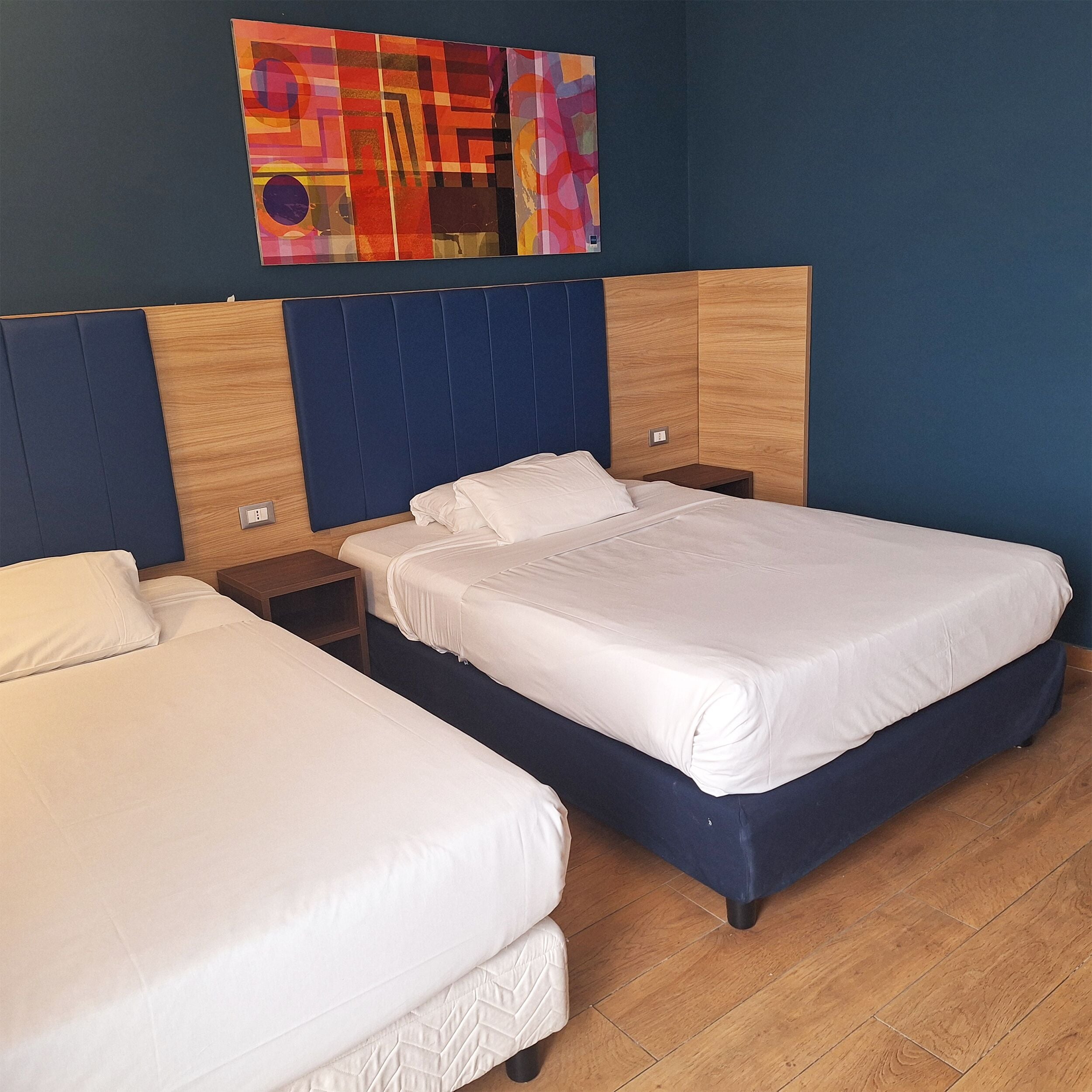 A hotel room with a large bed, a smaller bed, a wooden headboard, a nightstand, and a colorful abstract painting on the wall.