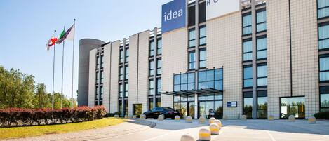 Egy modern hotel, amelyen feltűnő „ötlet” felirat látható, fedett bejárattal és oszlopokkal határolt parkolóval.