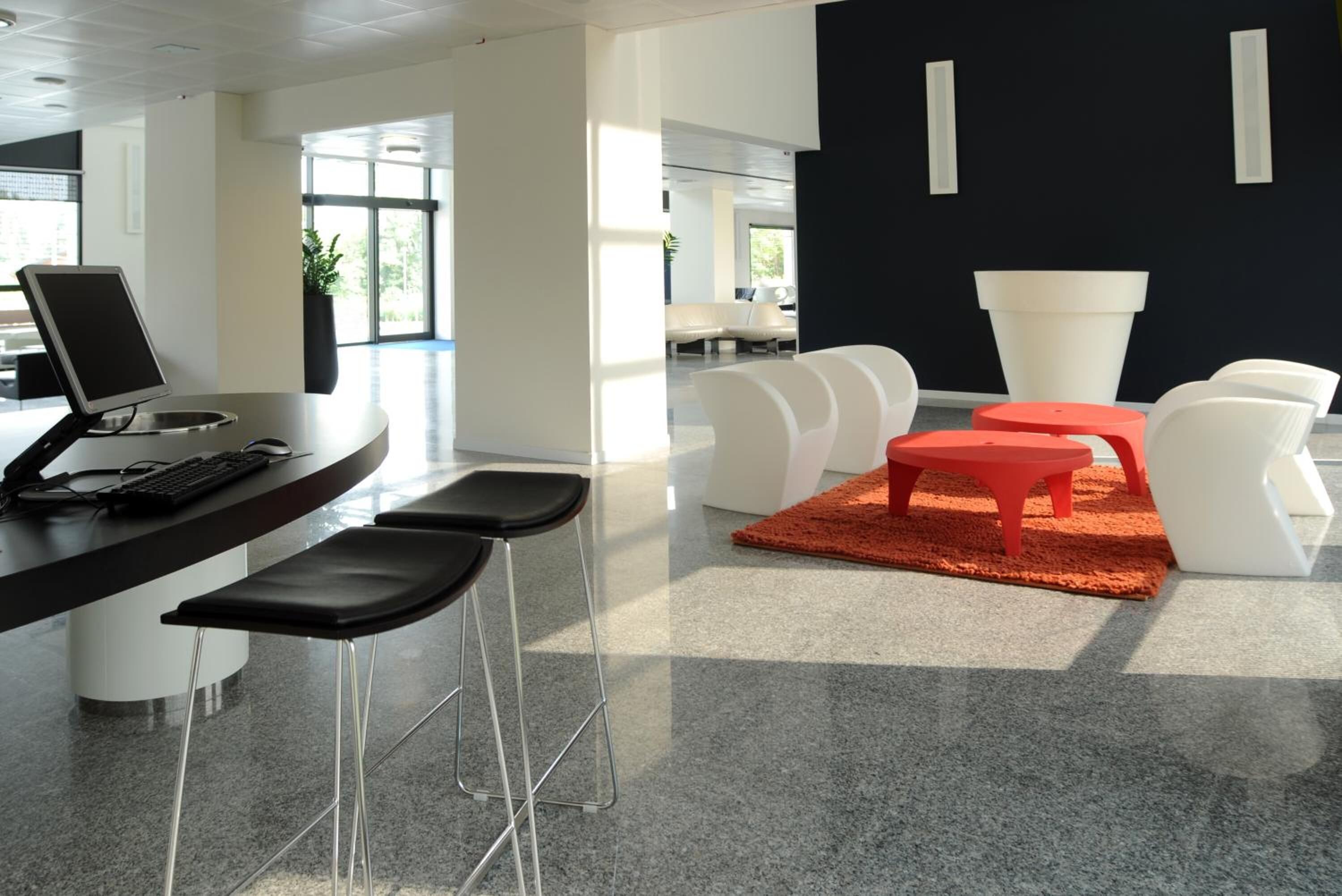 A modern office space with a curved desk, black and white chairs, and a red rug.