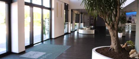 Un moderno vestíbulo de hotel con amplias ventanas, un mostrador de recepción y una palmera en una maceta.