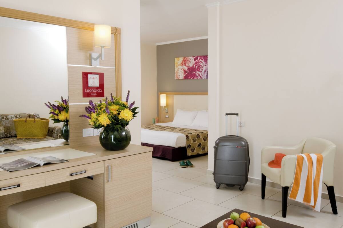 Een hotelkamer met een bed, een bureau met een spiegel, een stoel, een koffer en een schaal fruit.