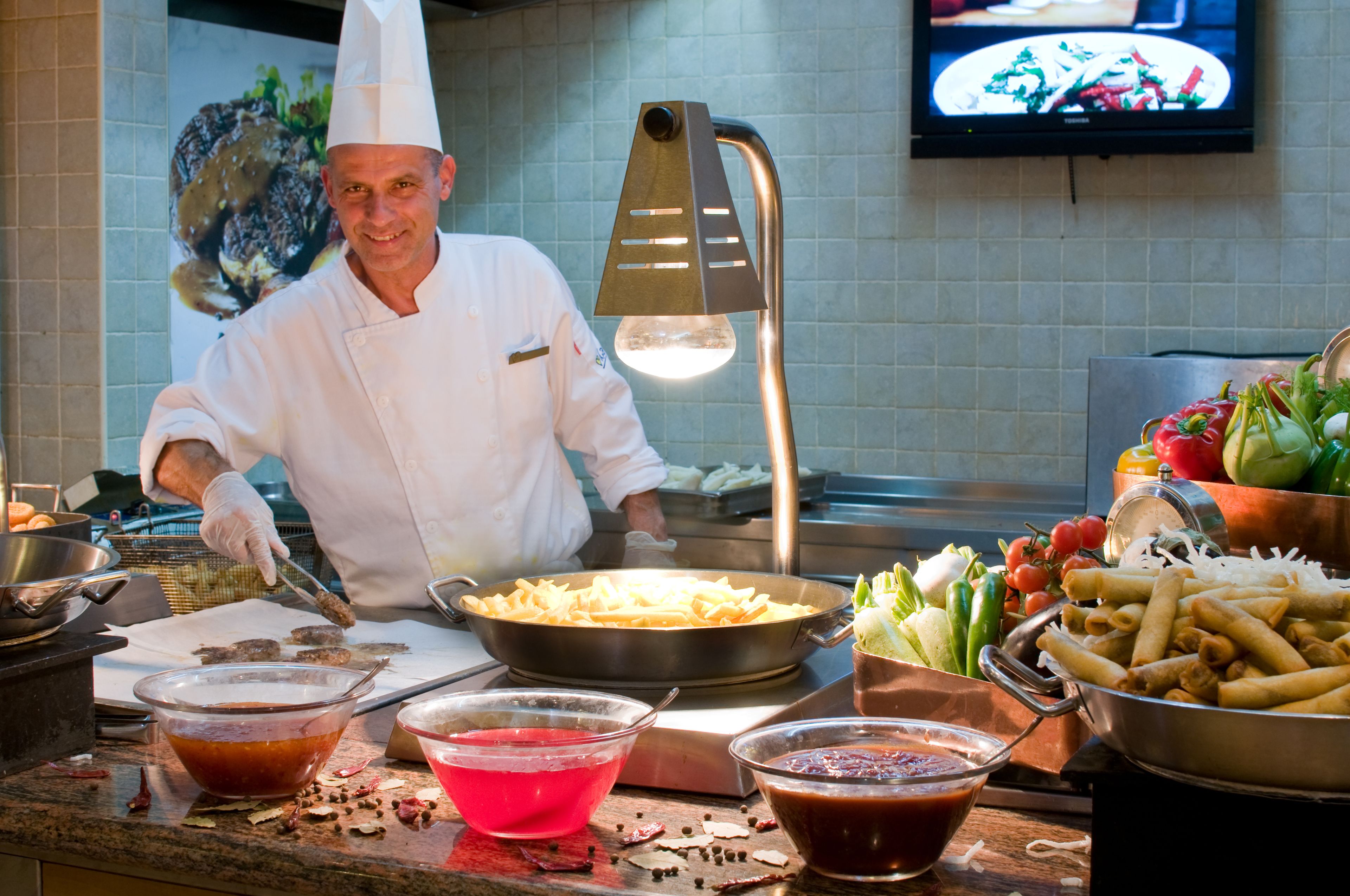 A chef in a white uniform cooking at a buffet station with various dishes and condiments.