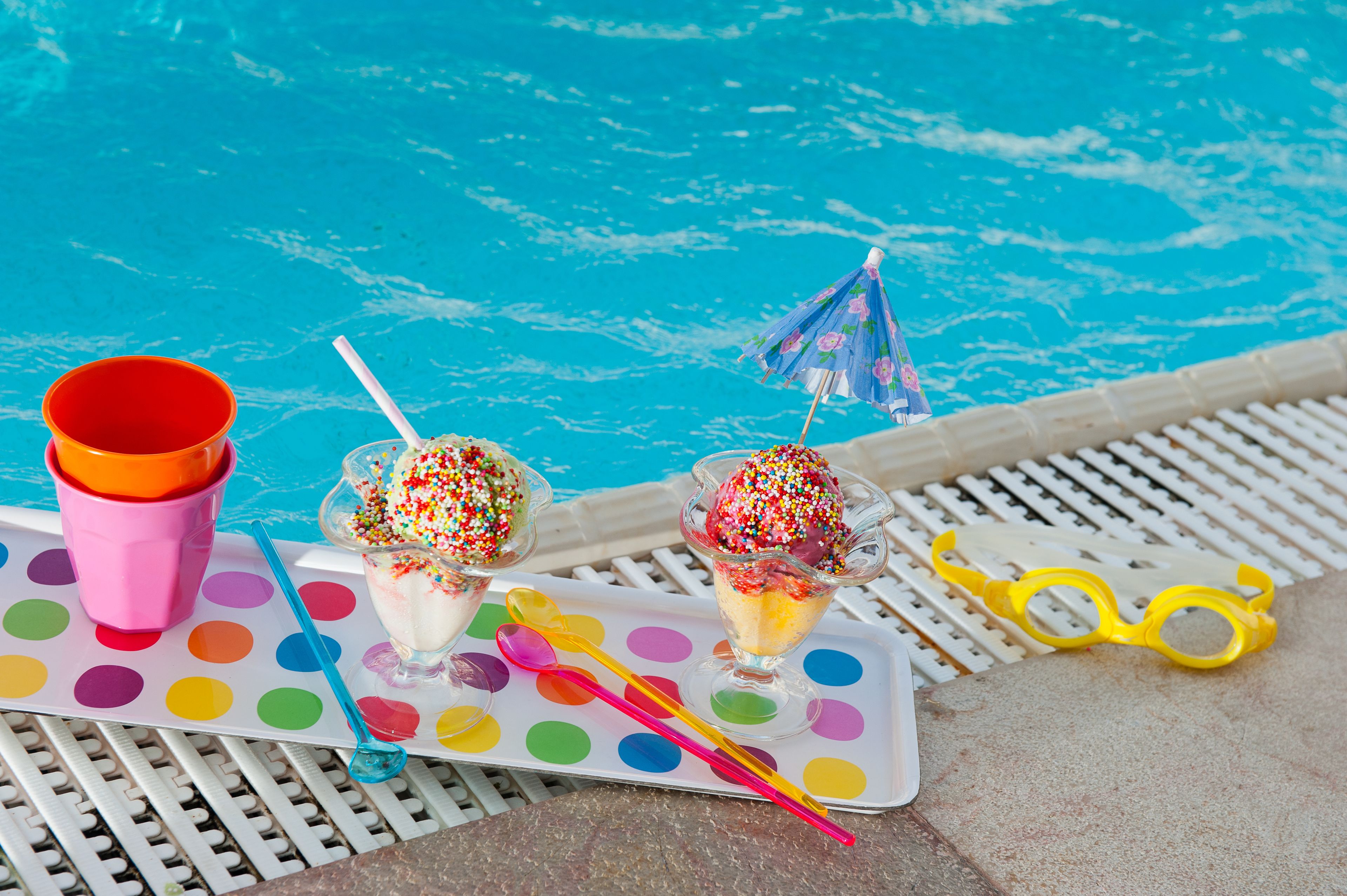 A poolside setting with a polka dot tablecloth, a pink cup, and two ice cream cones with sprinkles.