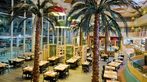 A spacious indoor restaurant with high ceilings, palm trees, and a modern design. - Leonardo Royal Resort Hotel Eilat (Eilat)