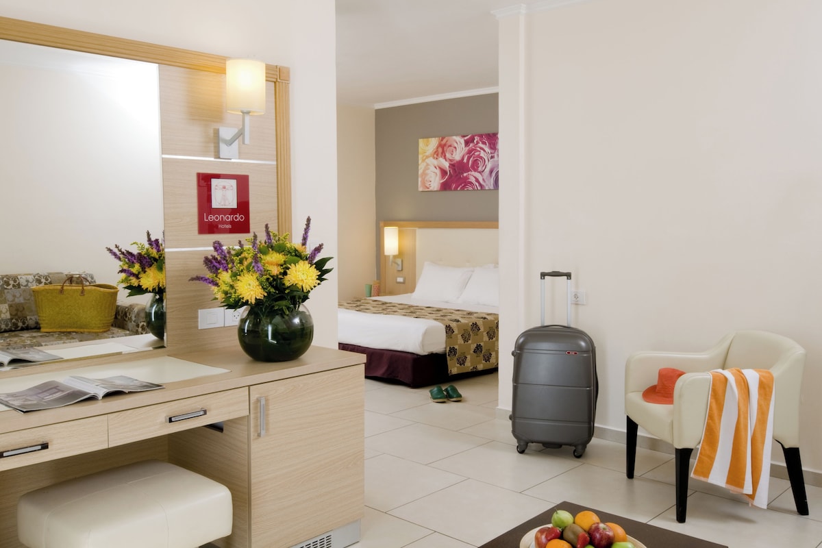 Habitación de hotel con cama, escritorio con espejo, silla, maleta y frutero.