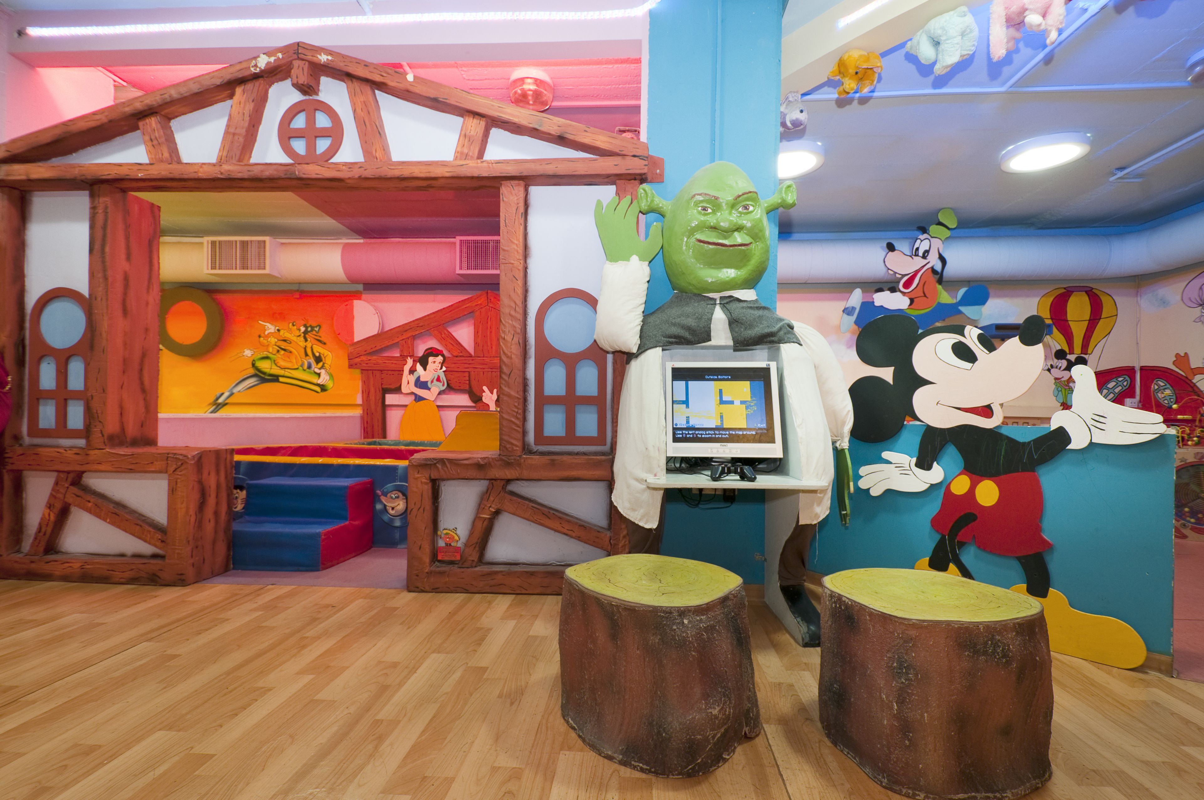 Een speelruimte voor kinderen met een houten poppenhuis, een groot Shrek-beeld en Mickey Mouse-decoraties.