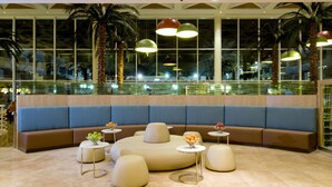 A modern lounge area with a curved seating arrangement, small round tables, and a glass railing overlooking a reflective pool. - Leonardo Royal Resort Hotel Eilat (Eilat)