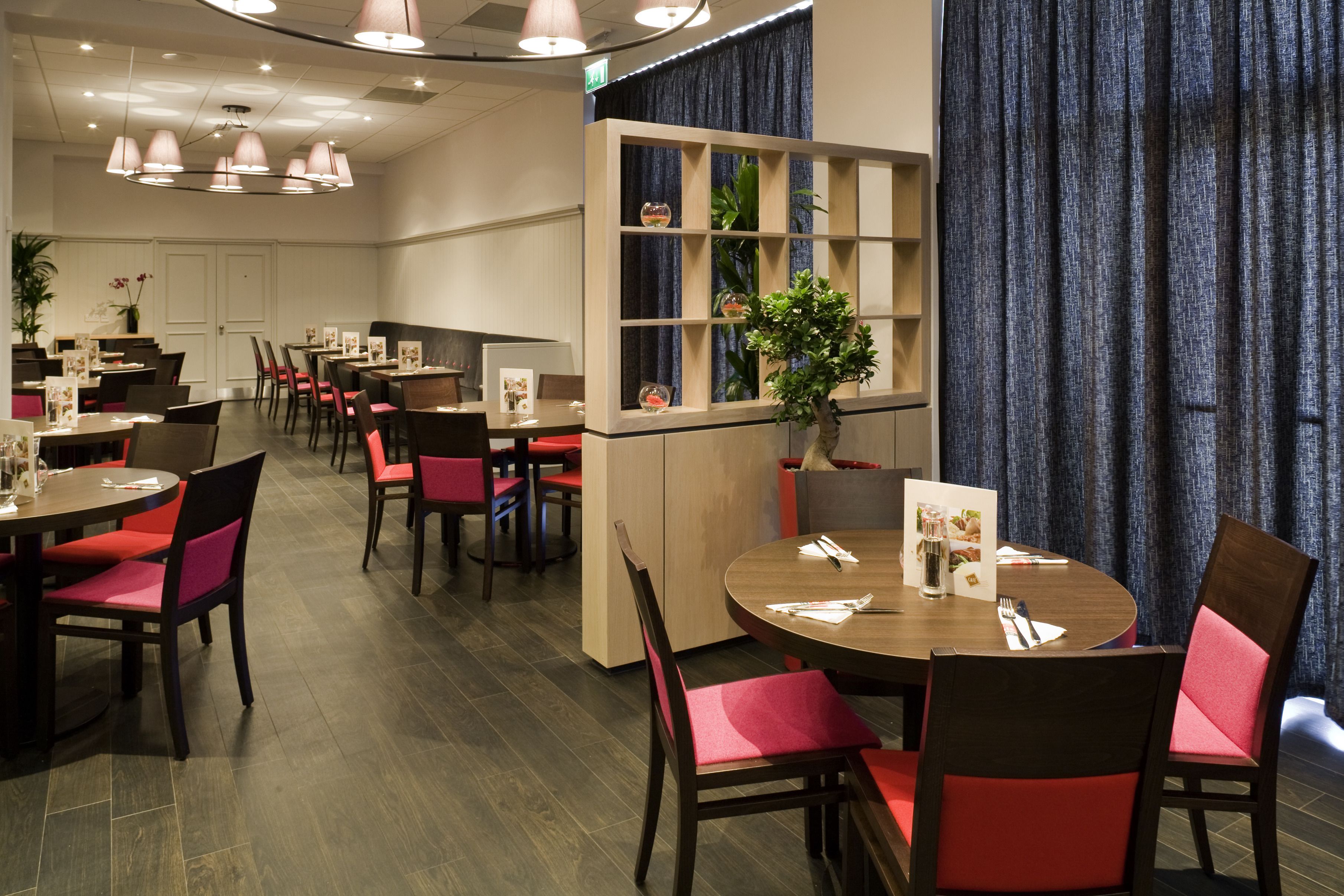 Un restaurante con mesas redondas y sillas rojas, una barra de madera y una cortina azul.