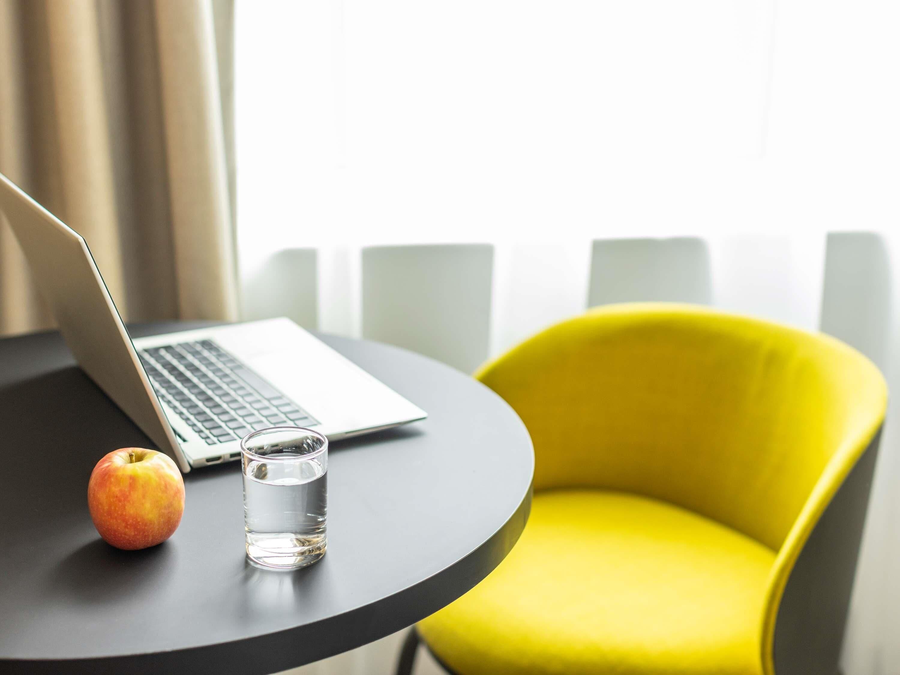 A laptop on a table with an apple and a glass of water.