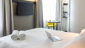 Una habitación de hotel con una cama, una computadora portátil, un televisor y una mesita con una silla.