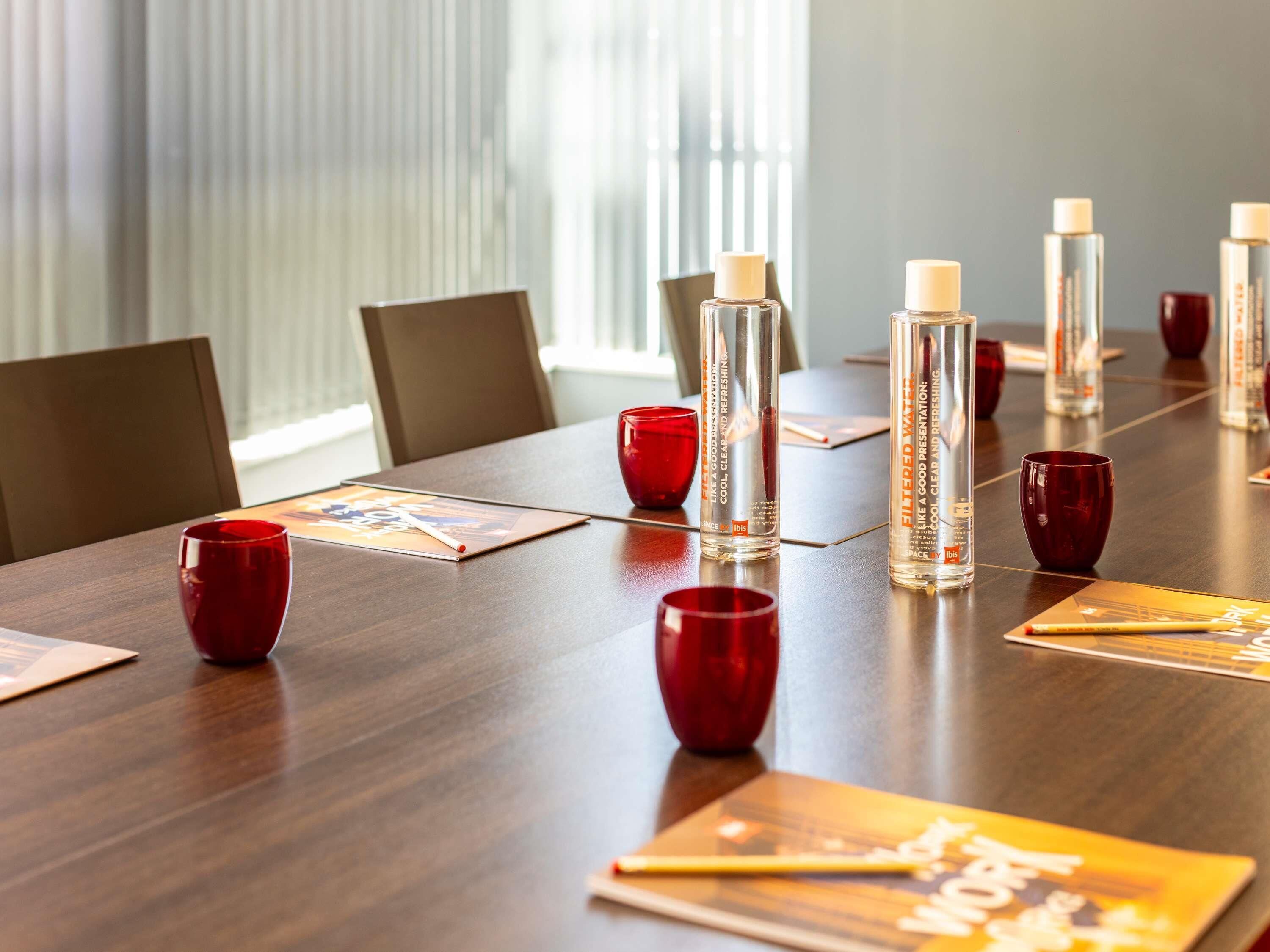Une table de conférence avec des bouteilles d’eau, des verres rouges et un magazine.