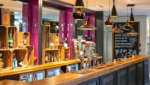 Zona de bar con estantes de madera mostrando botellas, una barra con grifos y un menú en la pizarra que detalla bebidas.