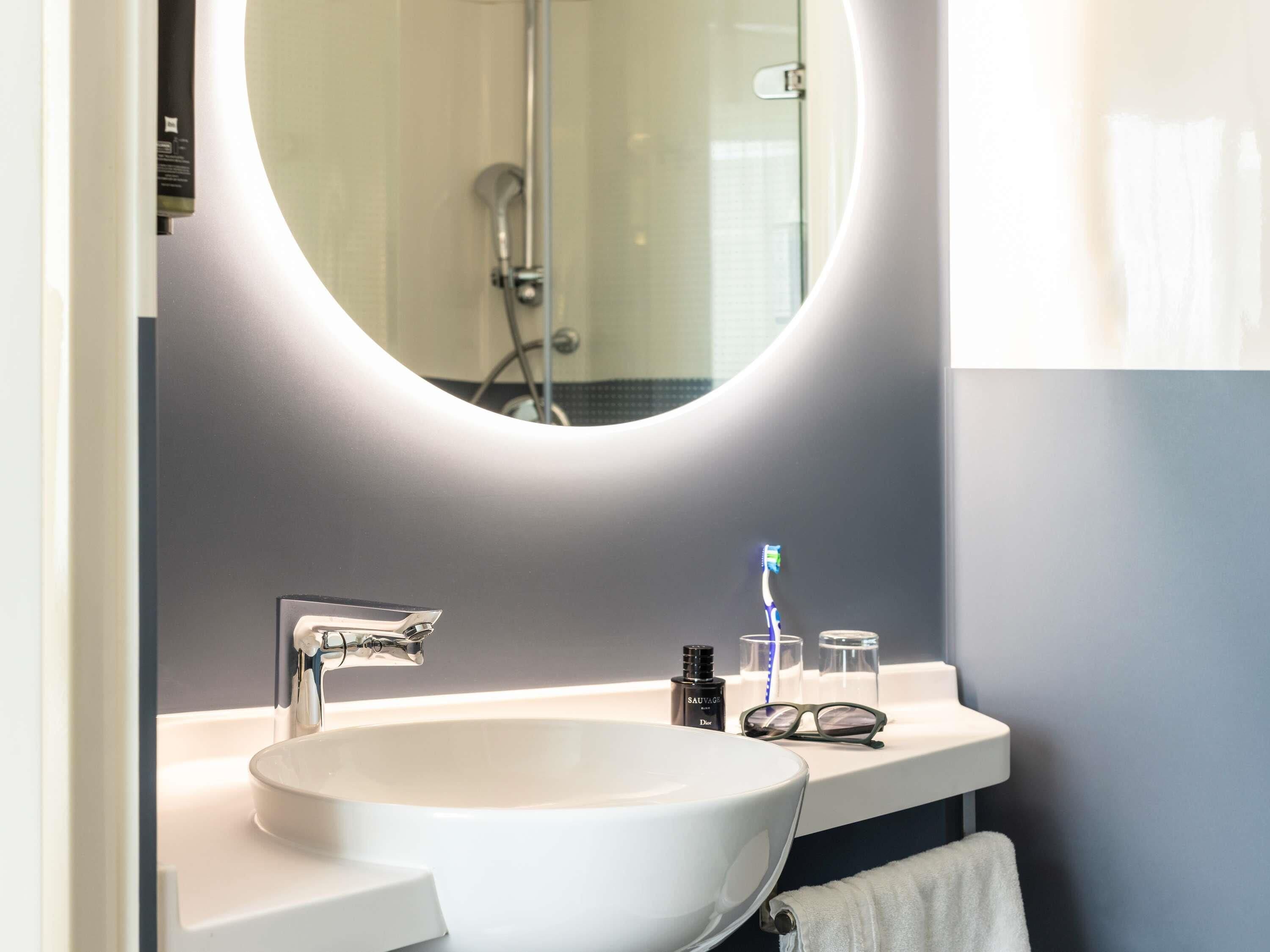 A modern bathroom with a round mirror, a white sink, and a shower.