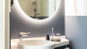 A modern bathroom with a round mirror, a white sink, and a shower.