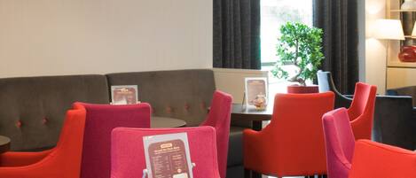 Zona pranzo di un hotel con sedie rosse imbottite, un tavolo rotondo e un espositore per i menu.