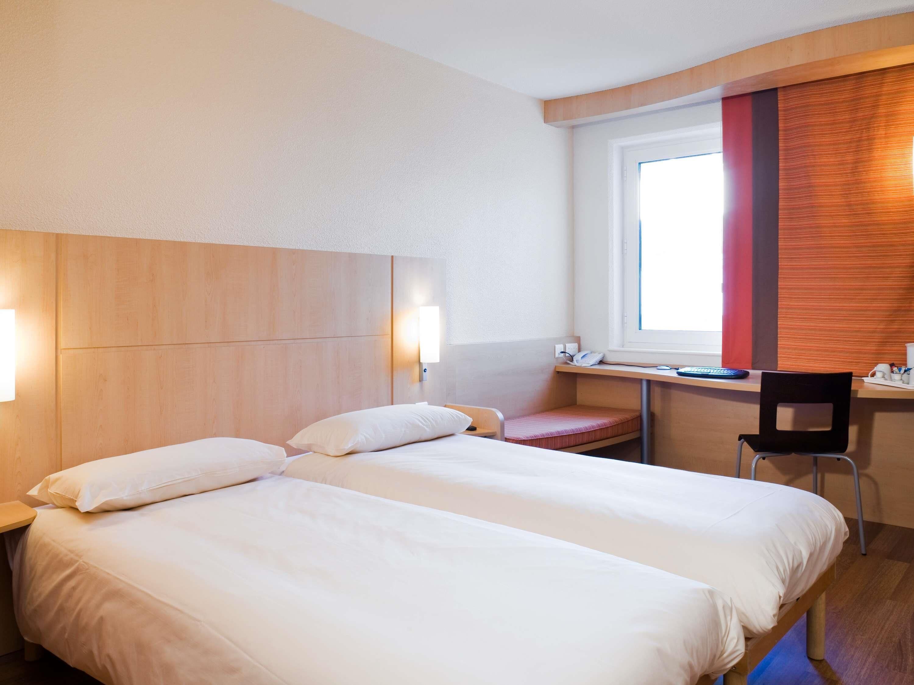Een hotelkamer met twee bedden, een bureau en een stoel.