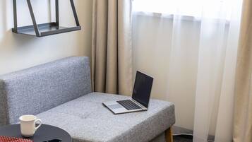 A grey sofa with a laptop, a white mug, and a red patterned cloth on a small round table.
