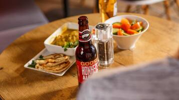 Una mesa de madera con una botella de Goose Island Hot Ales, un tazón de ensalada, un plato de comida y un salero.