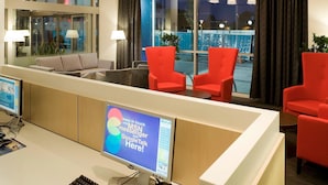 Zona de recepción de un hotel con un mostrador, computadora y dos sillas rojas.