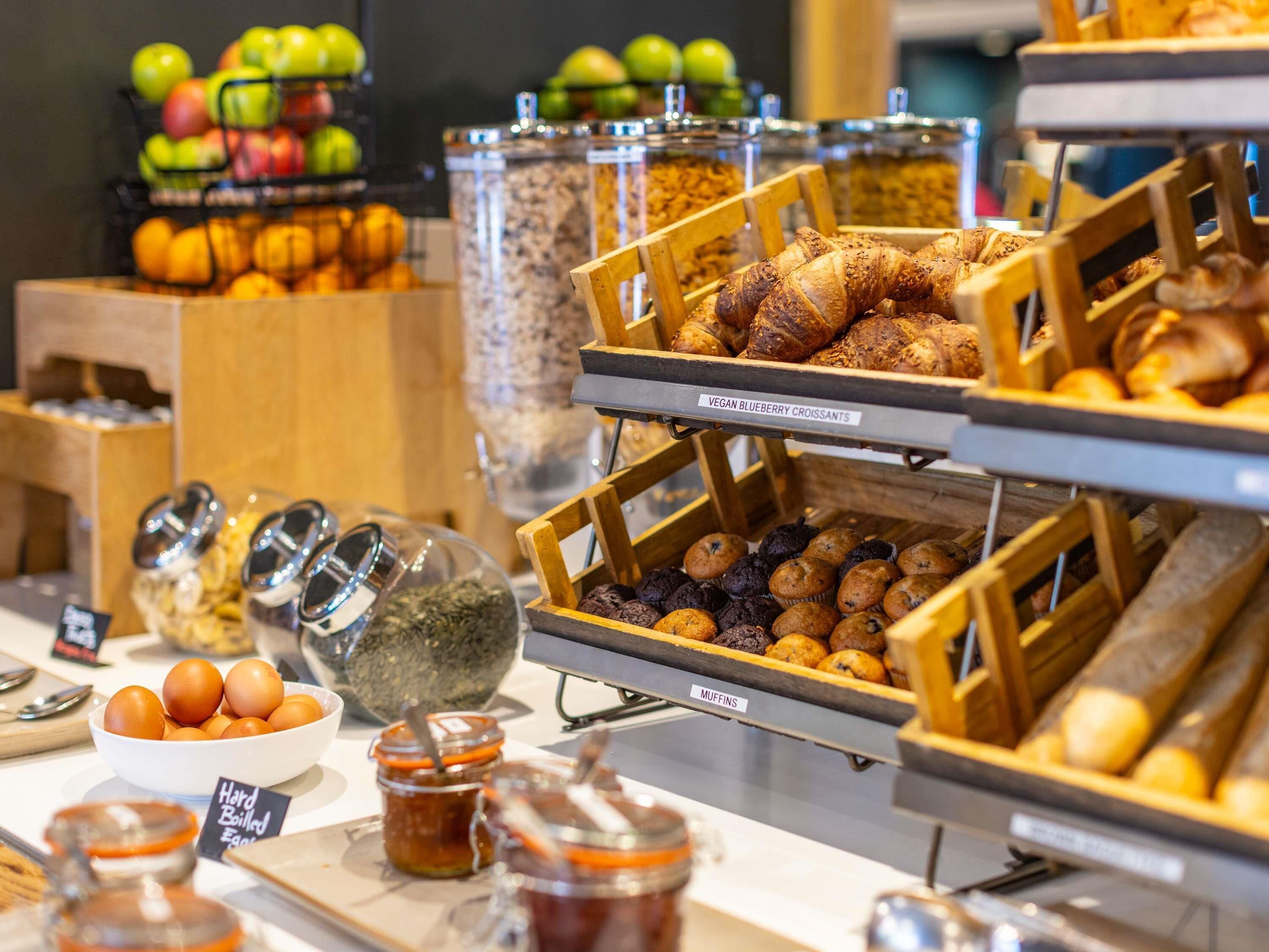 A breakfast buffet with various food items including muffins, croissants, and hard-boiled eggs.