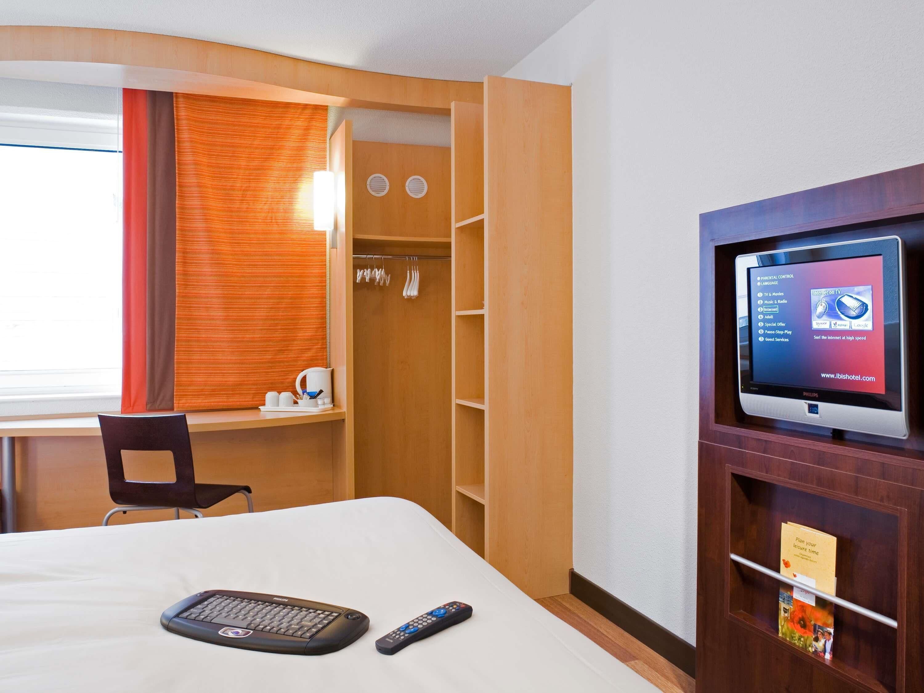 A hotel room with a bed, a desk, a chair, a television, and a wardrobe.