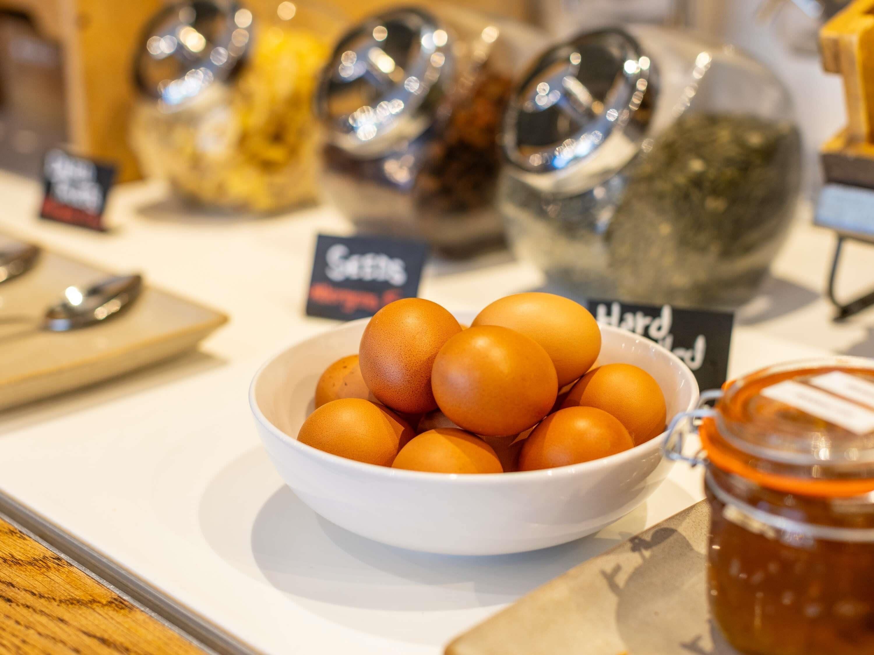 Un bol d’œufs sur une table, avec des pots de condiments en arrière-plan.