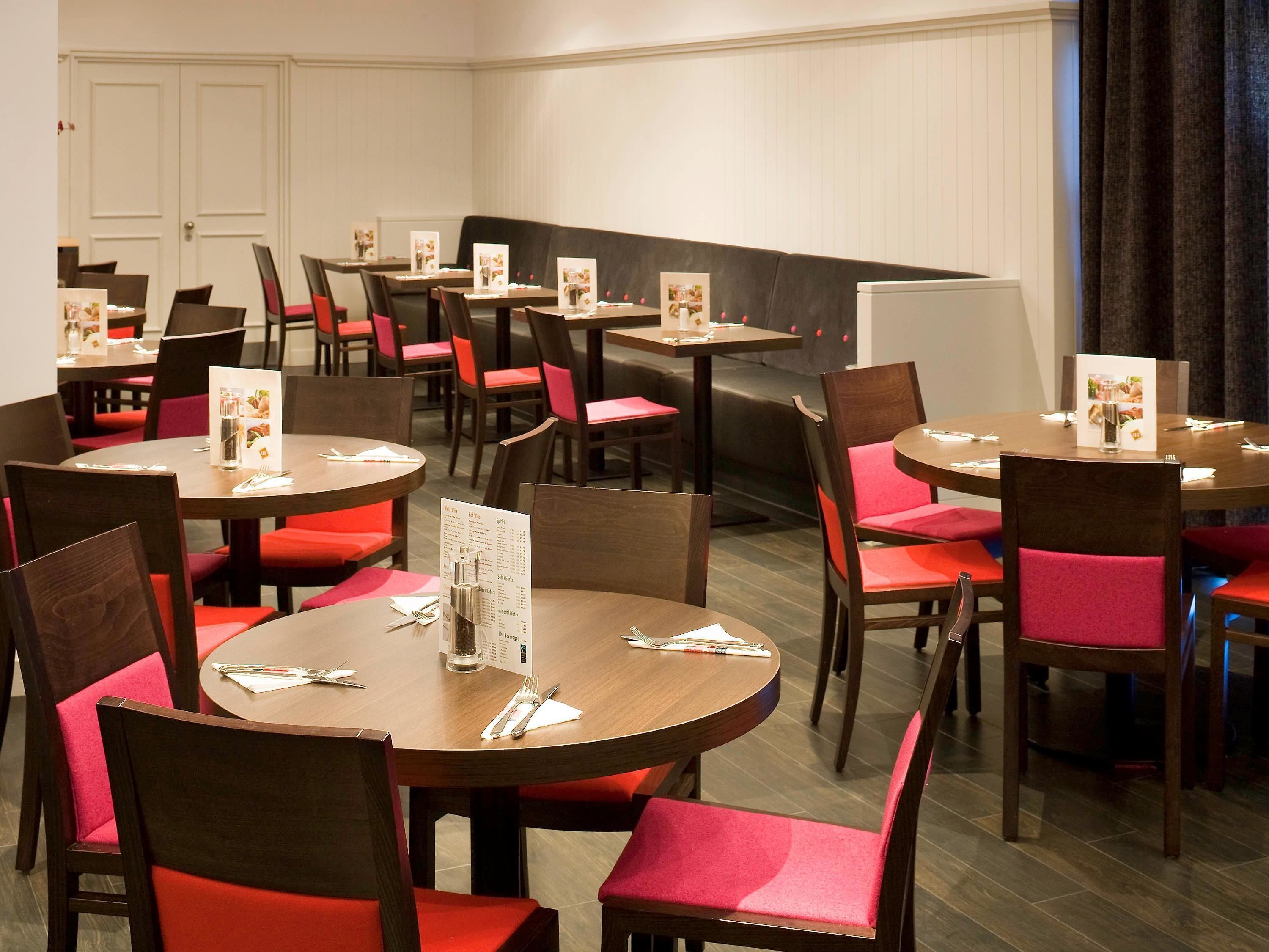 A restaurant with round tables and red cushioned chairs, featuring menus and a whiteboard.