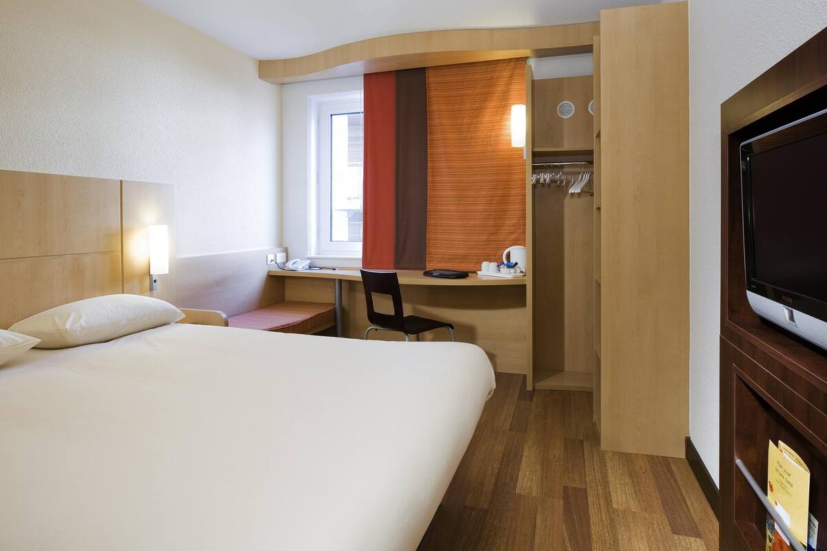A hotel room with a bed, desk, chair, TV, and a walk-in closet.