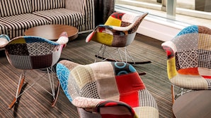 Una habitación de hotel moderna con un sofá a rayas, una mesa de centro redonda de madera y tres sillones de estilo patchwork.