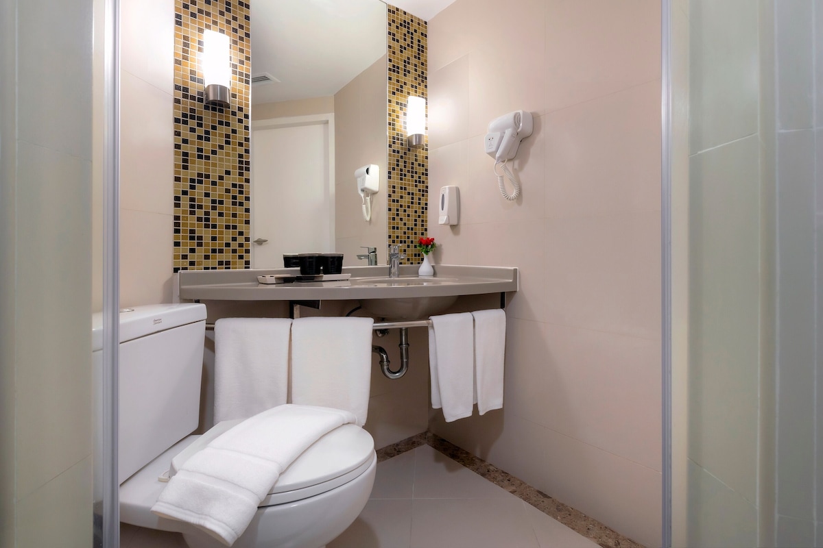 A bathroom with a toilet, sink, and mirror. There are towels hanging on the wall and a shower curtain.