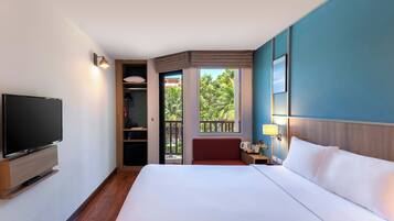 Quarto de hotel com cama, televisão, guarda-roupa e varanda com vista para o verde.