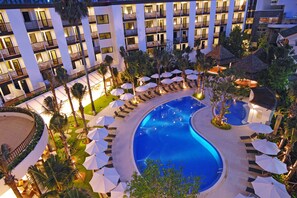 A hotel with a large swimming pool surrounded by lounge chairs and umbrellas, multiple floors with balconies, and a well-lit exterior. - ibis Phuket Patong (Patong)
