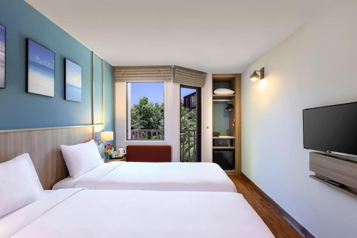 A hotel room with two beds, a TV, a balcony with a view, and a small table with a vase of flowers.