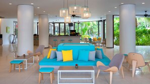 Un área de estar moderna con un sofá azul, sillas de madera, una mesa de centro e iluminación colgante.